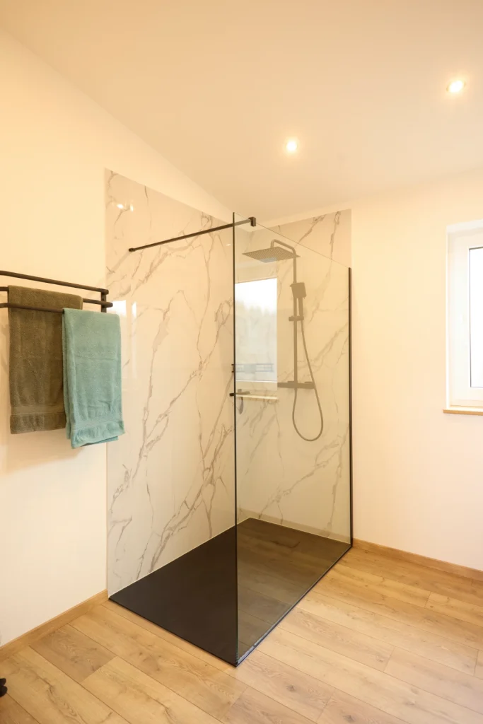Große Dusche mit Glaswand, Wandverkleidung in Marmoroptik und schwarzer Regendusche