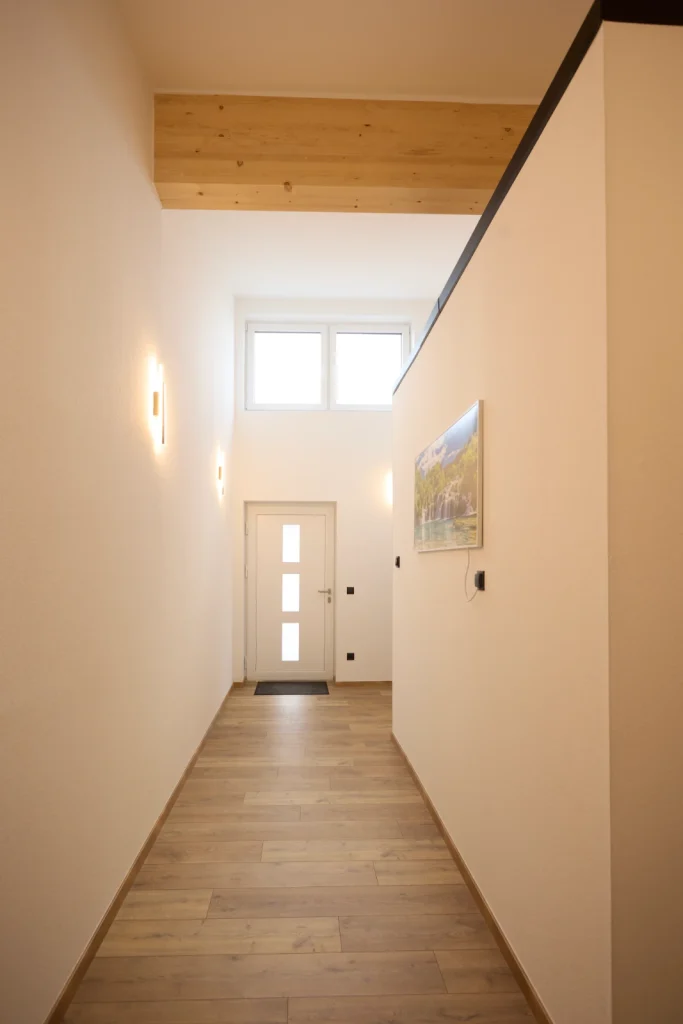 Heller Eingangsflur mit hoher Decke, Holzbalken und Fenster über der Haustür