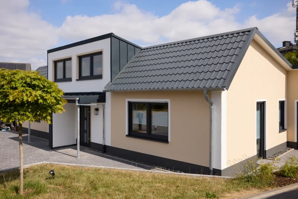 Seitenansicht des Hauses mit Satteldach, Rasenfläche und Baum vor dem Eingang