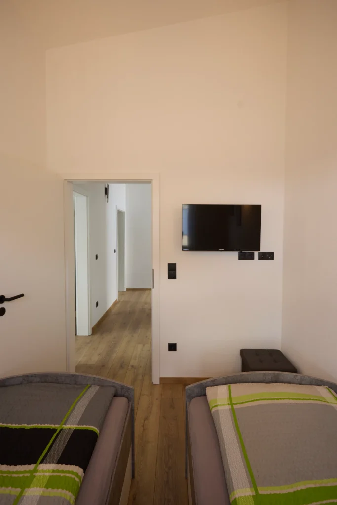 Blick von den Einzelbetten auf Fernseher und Tür zum Flur